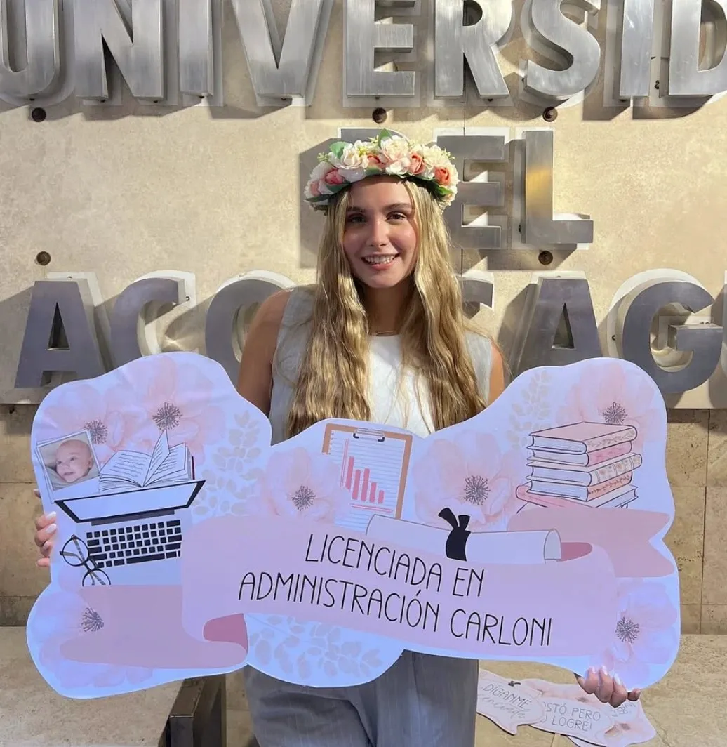 Julieta Carloni con corona de flores en su graduación, sosteniendo un cartel que dice Licenciada en Administración