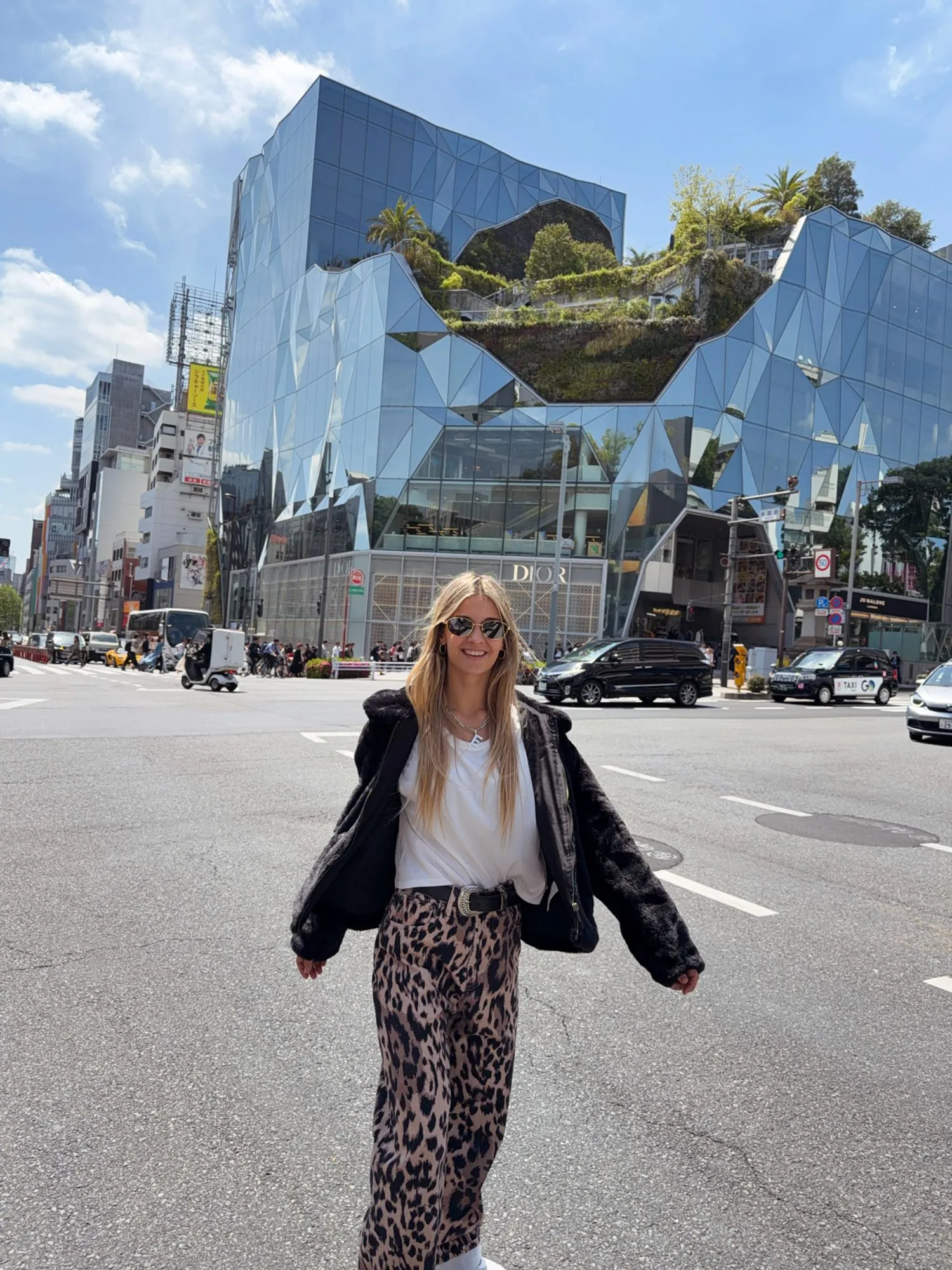 Emi Estoco caminando por una avenida de Tokio, frente a un edificio de espejos