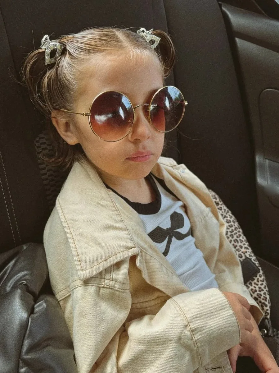 Alma con anteojos de sol redondos, campera beige y hebillas brillantes en el auto