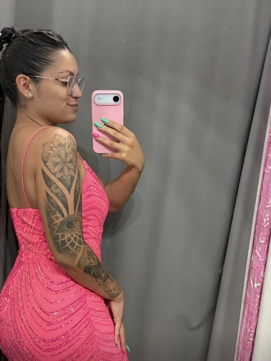 Juli con un vestido rosa de brillos, sacándose una selfie en el espejo de un probador